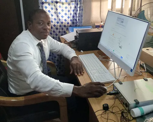 Johnson Olowe is photographed sitting at a desk using Lt LabStation on a desktop computer. A PowerLab unit sits beside the computer.