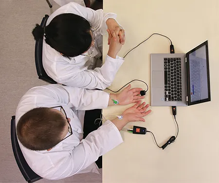 A birds-eye view photo of two students working on a laptop in a laboratory setting. A Biopotential Lt Sensor and a Finger Pulse Lt Sensor are connected to the laptop and one of the students.