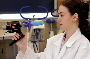 A student holds the Lt Sensors Spirometer in one hand in a laboratory setting.