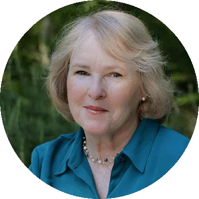 A photograph of Professor Dee Silverthorn. She has blonde short hair, wears a blue shirt, and is smiling at the camera against a background of greenery.