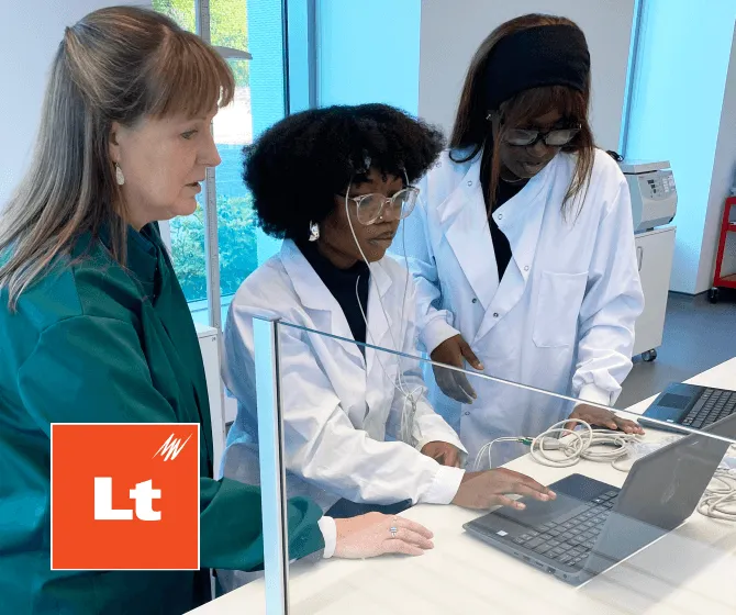 Dr. Ann Rajnicek is pictured in the lab helping two students in white lab coats to perform EEG using a laptop.